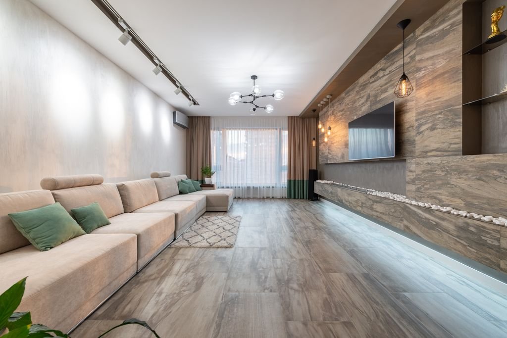 Interior of living room with long comfortable sofa with green pillows placed near wall opposite TV in modern apartment
